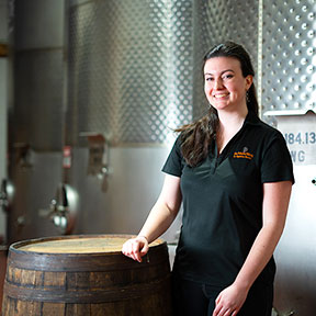 Young femail sommelier standing next to a wine barrell